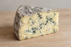 Cut wedge of soft blue-veined cheese with a grey natural rind on a wooden board - Montagnolo | KnowTheCheese