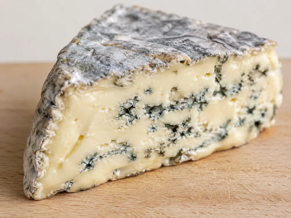 Cut wedge of blue-veined cheese showing a grey natural rind and cream-coloured paste with blue-green veining - Montagnolo | KnowTheCheese