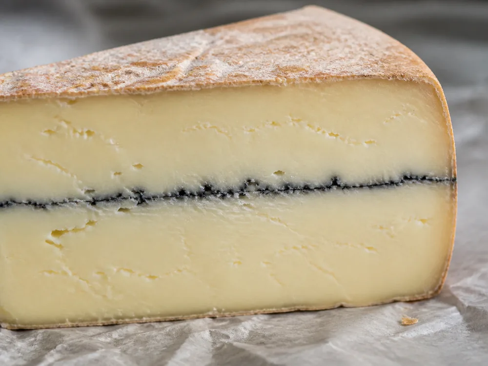 Close cross-section of Morbier-style cheese with a thin centered ash line - Morbier | KnowTheCheese