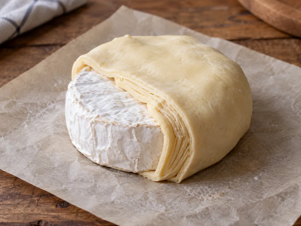 Round white bloomy-rind cheese half wrapped in raw puff pastry on baking parchment - Moses Sleeper | KnowTheCheese