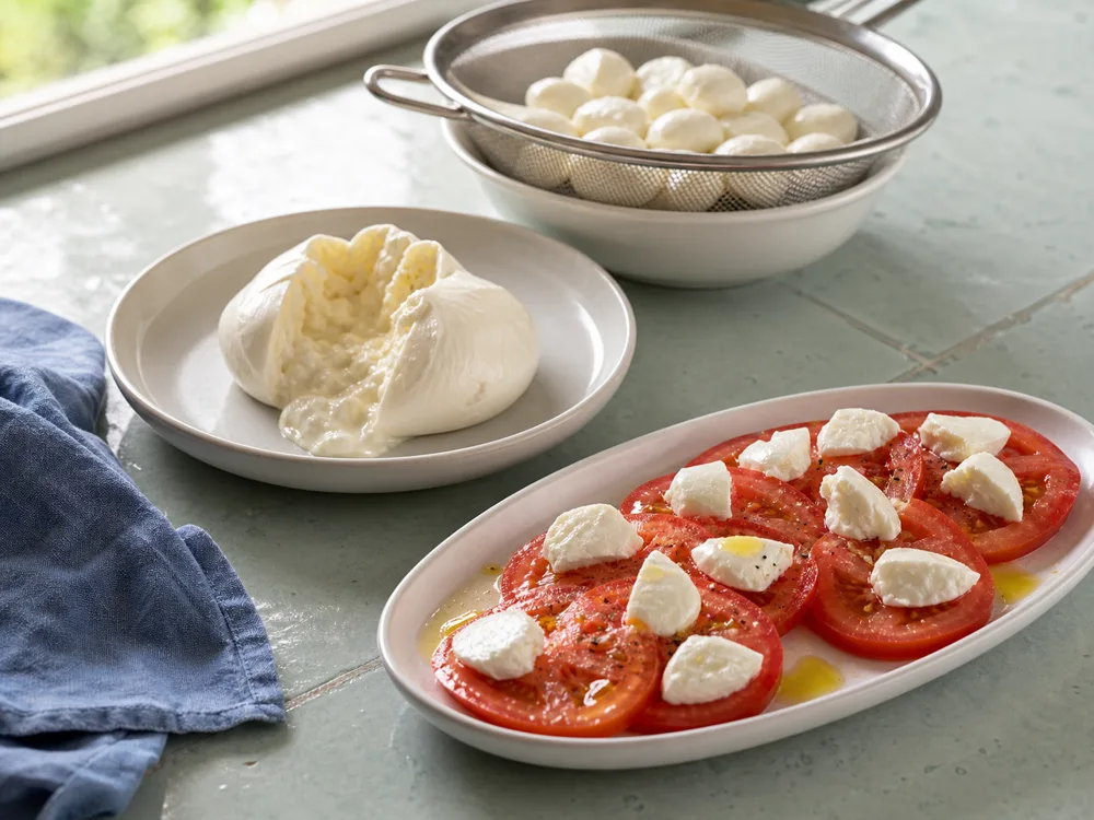 Bocconcini draining beside opened burrata and a tomato plate with fresh cheese - Mozzarella substitutes | KnowTheCheese