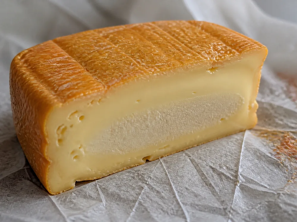 Cut Munster-style wedge showing orange rind and creamy pale center - Munster | KnowTheCheese