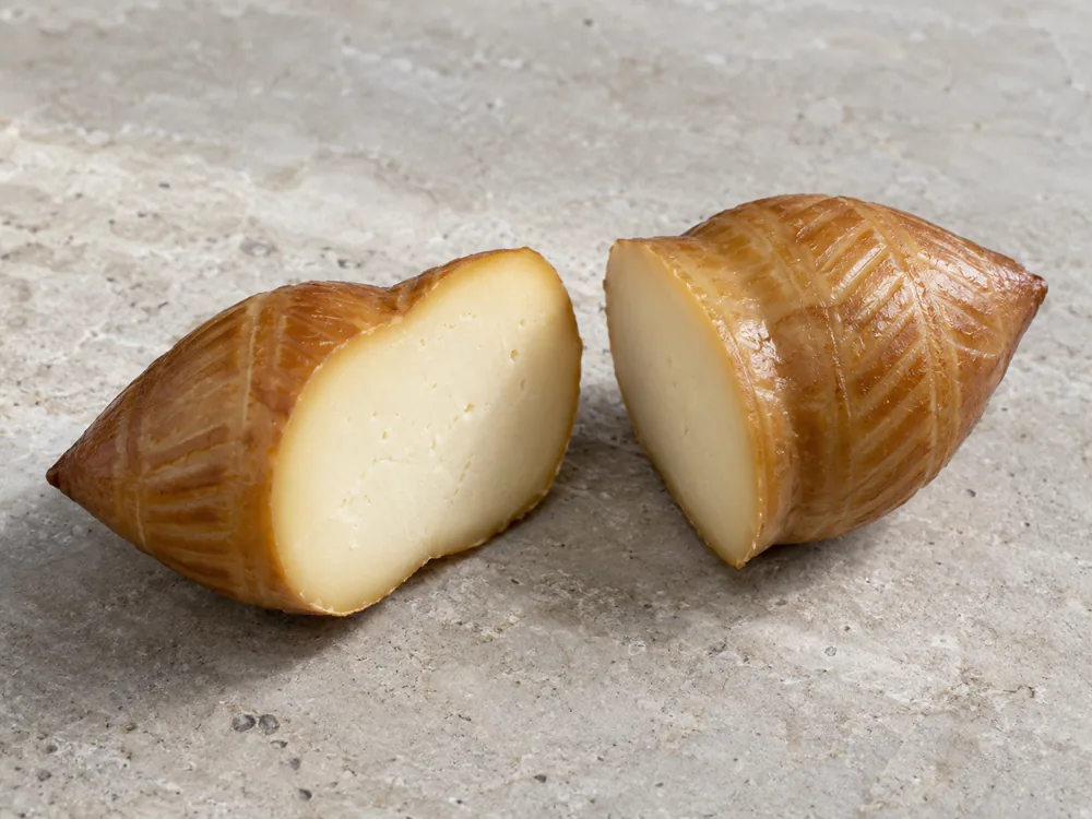 Smoked spindle-shaped cheese cut in two to show a creamy interior and glossy light-brown rind - Oscypek | KnowTheCheese