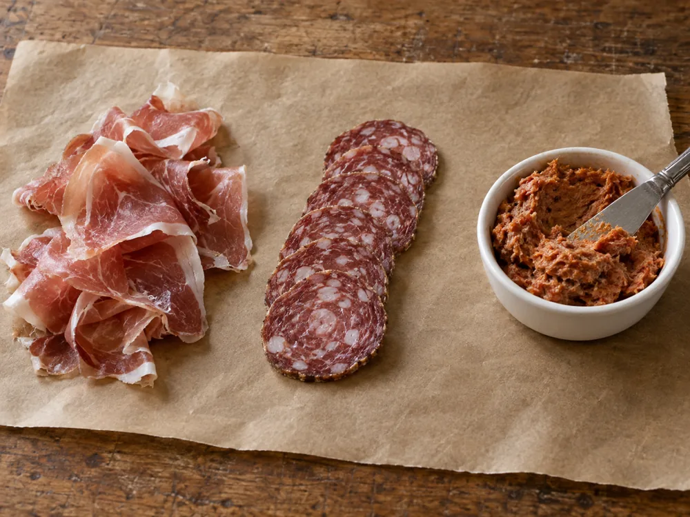 Thin ham slices, sausage rounds, and a dish of spreadable cured pork - cured meat styles | KnowTheCheese
