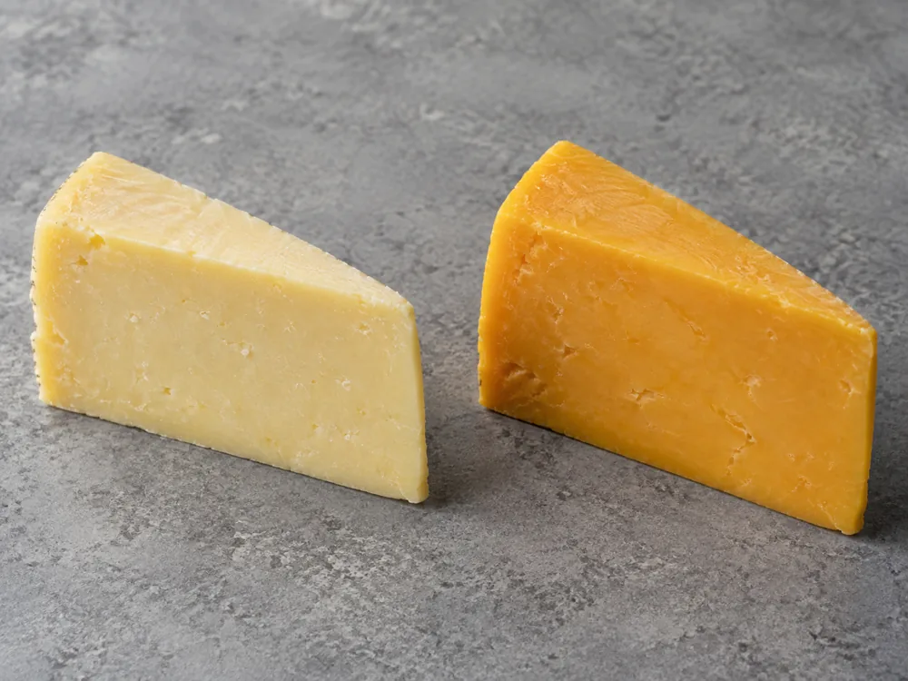 Two wedges of cheddar side by side, one off-white to pale yellow and one deep yellow-orange - Cheddar beer pairing | KnowTheCheese