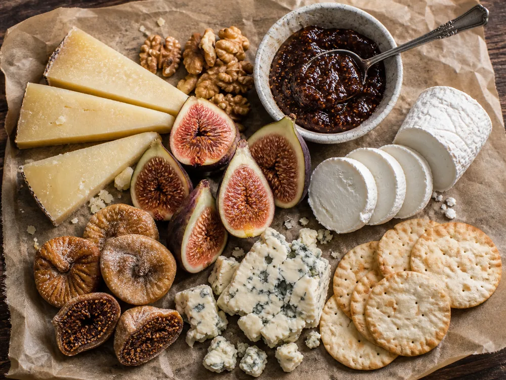 Fig and cheese board with fresh figs, dried figs, fig jam, goat cheese, blue cheese, aged firm cheese, walnuts, and crackers.