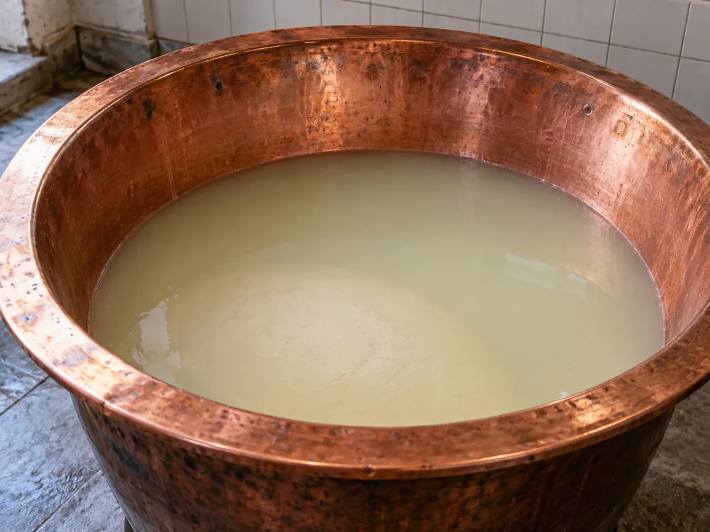 Bell-shaped copper cheese vat filled with cloudy whey - Parmigiano-Reggiano | KnowTheCheese
