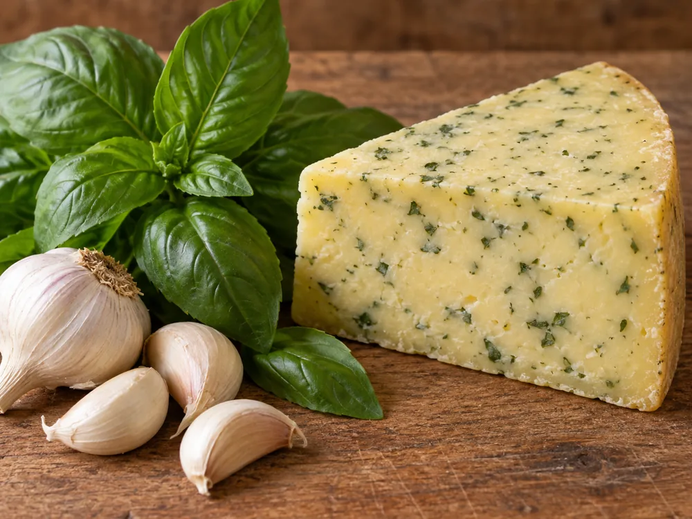 A wedge of Pesto Verde cheese beside fresh basil and garlic - Pesto Verde | KnowTheCheese