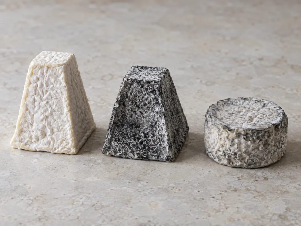 Three goat cheeses in a row: a white-rinded pyramid, an ash-coated pyramid and a grey round puck - Pouligny-Saint-Pierre | KnowTheCheese