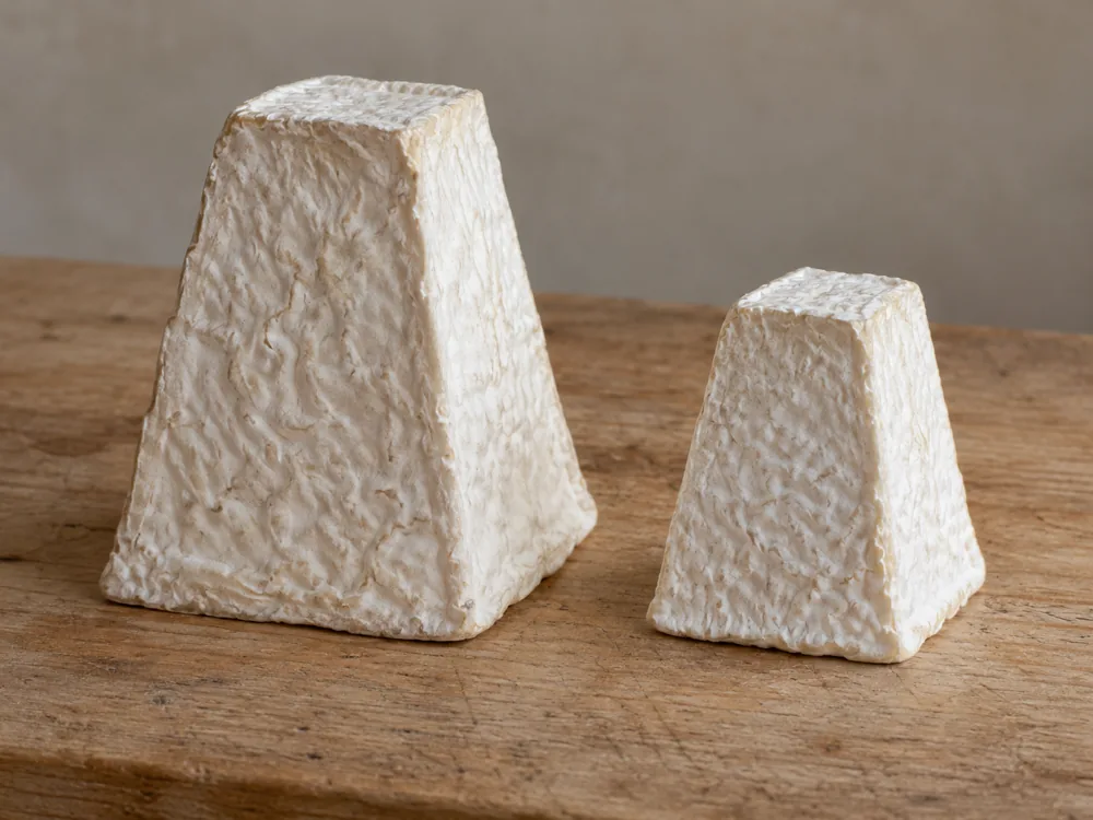 Two square-based goat cheese pyramids with wrinkled white rinds on a wooden board, one larger and one smaller - Pouligny-Saint-Pierre | KnowTheCheese
