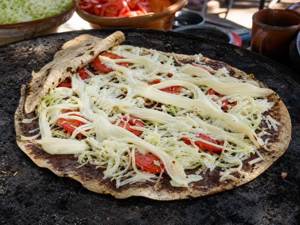 Quesillo ribbons melting across an open Oaxacan tlayuda - Quesillo | KnowTheCheese