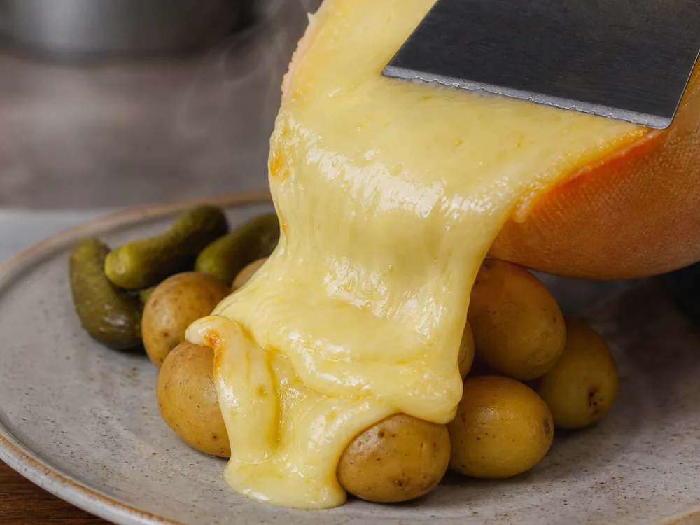 Melted Raclette being scraped over boiled potatoes - Raclette Cheese | KnowTheCheese