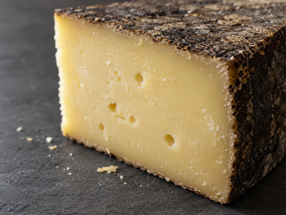 Cut corner of a hard cheese with a dry black-brown rind and smooth yellow-white paste with a few small holes - Rotwein Bargler Extra Wurzig | KnowTheCheese