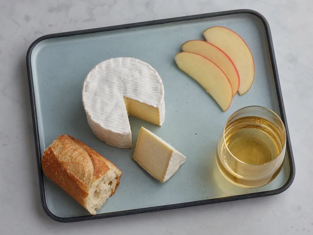 Saint-Andre with apple wedges, plain baguette, and dry cider on an enamel tray - Saint-Andre | KnowTheCheese