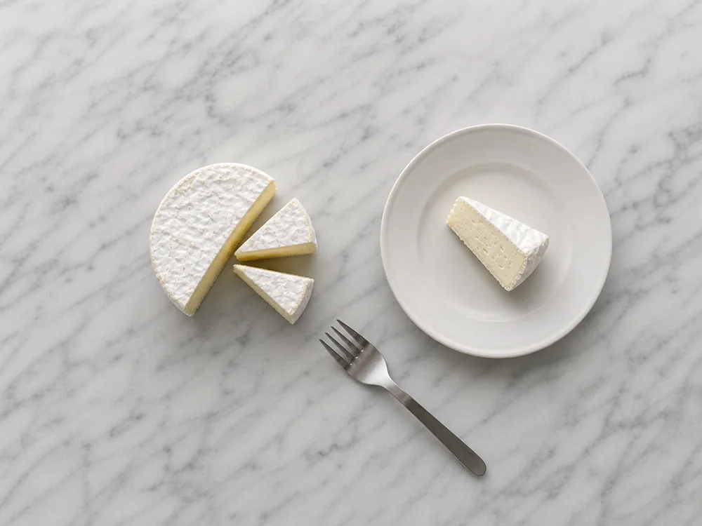 Compact Saint-Andre mini round cut into narrow serving wedges beside a dessert fork - Saint-Andre | KnowTheCheese
