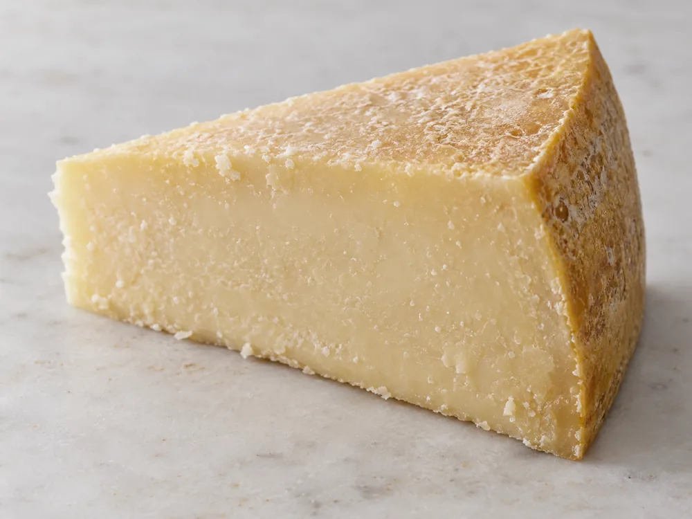 Wedge of extra-hard cheese with a closed pale cut face and a golden rind - Sbrinz cheese | KnowTheCheese