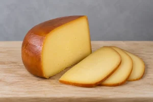 Smoked Gouda wedge with a darker brown outside and creamy yellow interior, three slices beside it - Smoked Gouda | KnowTheCheese