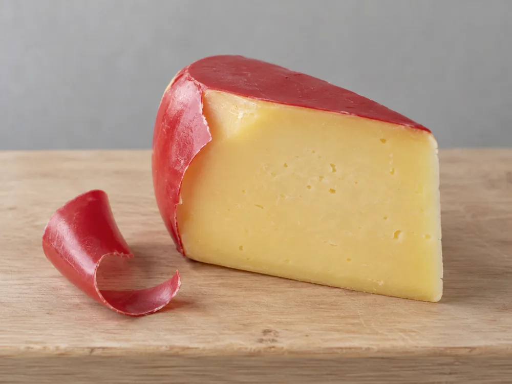 Pale yellow Gouda wedge with red wax peeled back from one corner and a curl of wax beside it - Smoked Gouda | KnowTheCheese