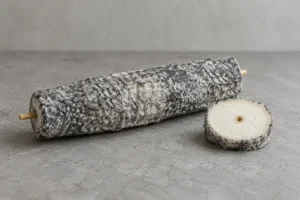 Tapered ash-coated Sainte-Maure de Touraine log with a cereal straw and one cut slice - Sainte-Maure de Touraine cheese | KnowTheCheese
