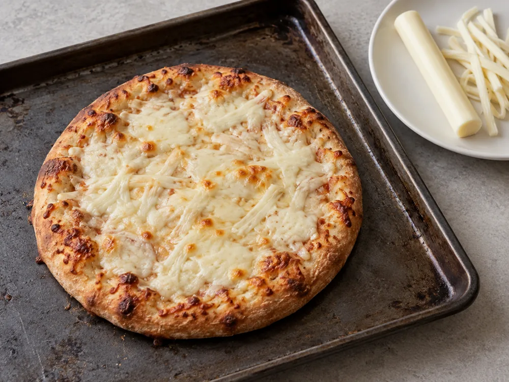 Baked pizza topped only with melted white cheese beside a string cheese stick and peeled strands - String cheese | KnowTheCheese