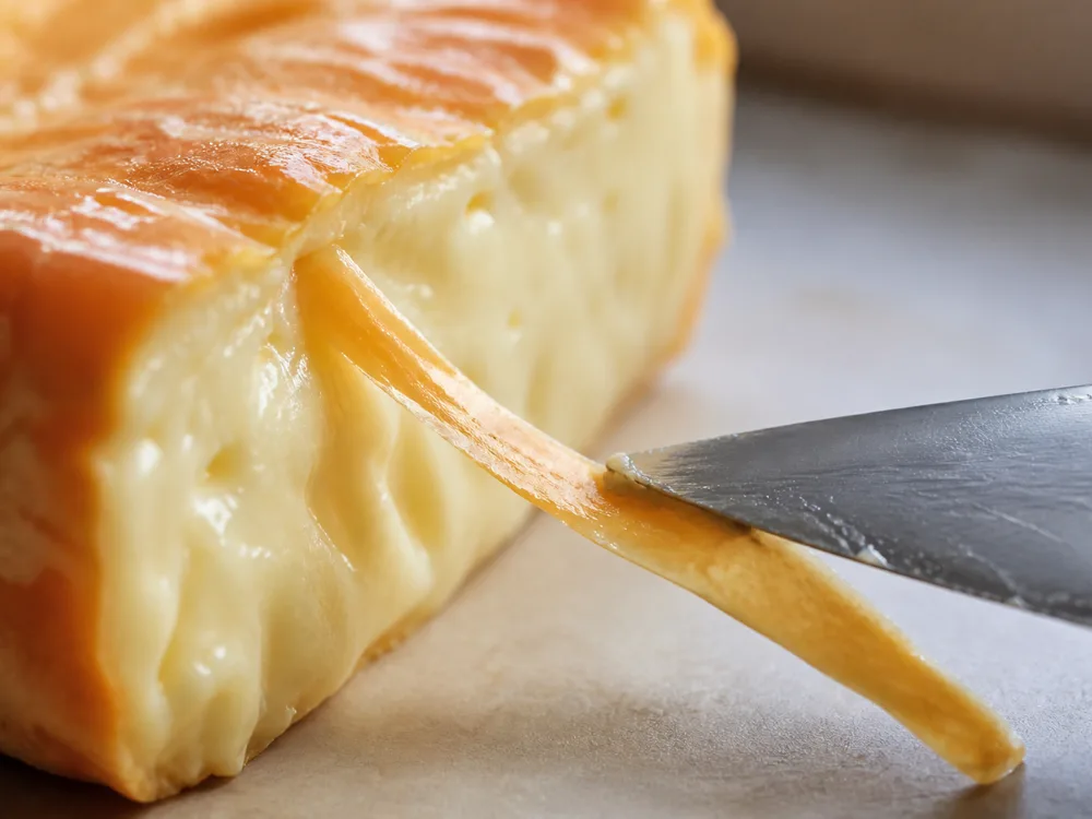 A knife separating a thin strip of washed rind from the paste of a cut wedge - Tamie | KnowTheCheese