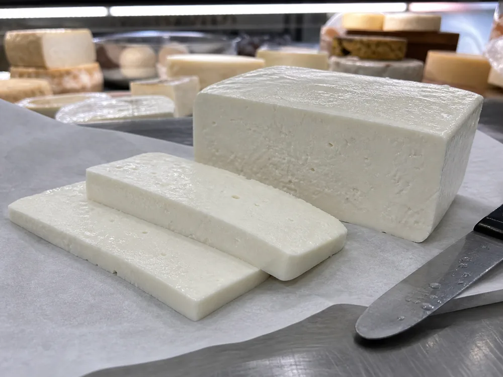 Teleme cheese block and thick slices on butcher paper at a deli counter