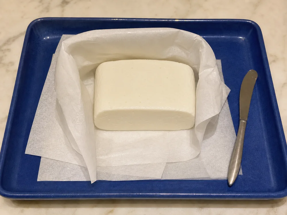 Teleme portion loosely folded in waxed cheese paper on a blue tray - Teleme | KnowTheCheese