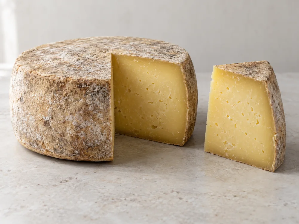 Whole round hard cheese with a natural rind and one wedge cut out and set beside it - Tezacki Sir Extra Mature | KnowTheCheese