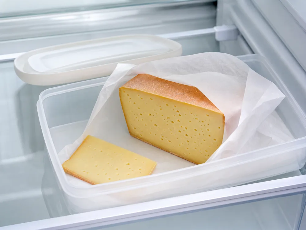Tilsiter wedge wrapped in cheese paper inside a refrigerator container - Tilsiter | KnowTheCheese