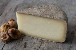 Wedge of Tomme with thick grey natural rind and pale paste - Tomme cheese | KnowTheCheese