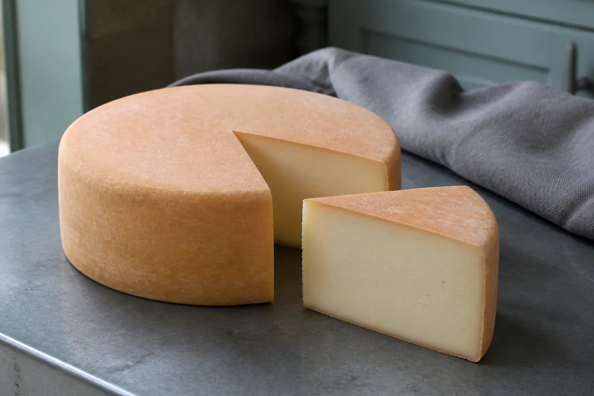 Straight-sided tomme with a thin orange rind and a cut wedge showing dense pale paste - Trappiste de Bricquebec | KnowTheCheese
