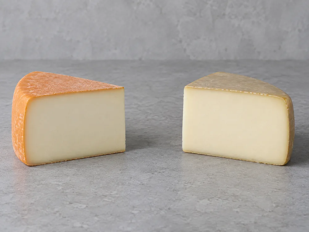 Two wedges of the same pale paste, one with an orange rind and one with a greyish-yellow rind - Trappiste de Bricquebec | KnowTheCheese