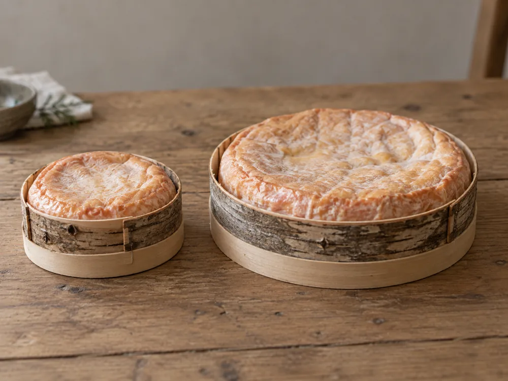 Smaller and larger soft cheeses held by bark straps in round wooden boxes
